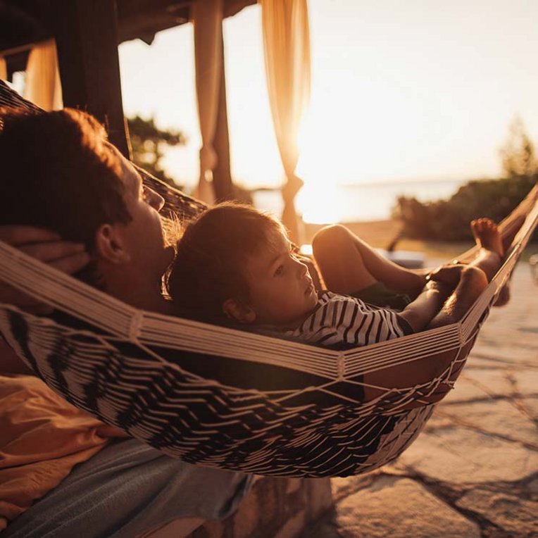 ein Vater und sein Sohn in einer Hängematte bei Sonnenuntergang.